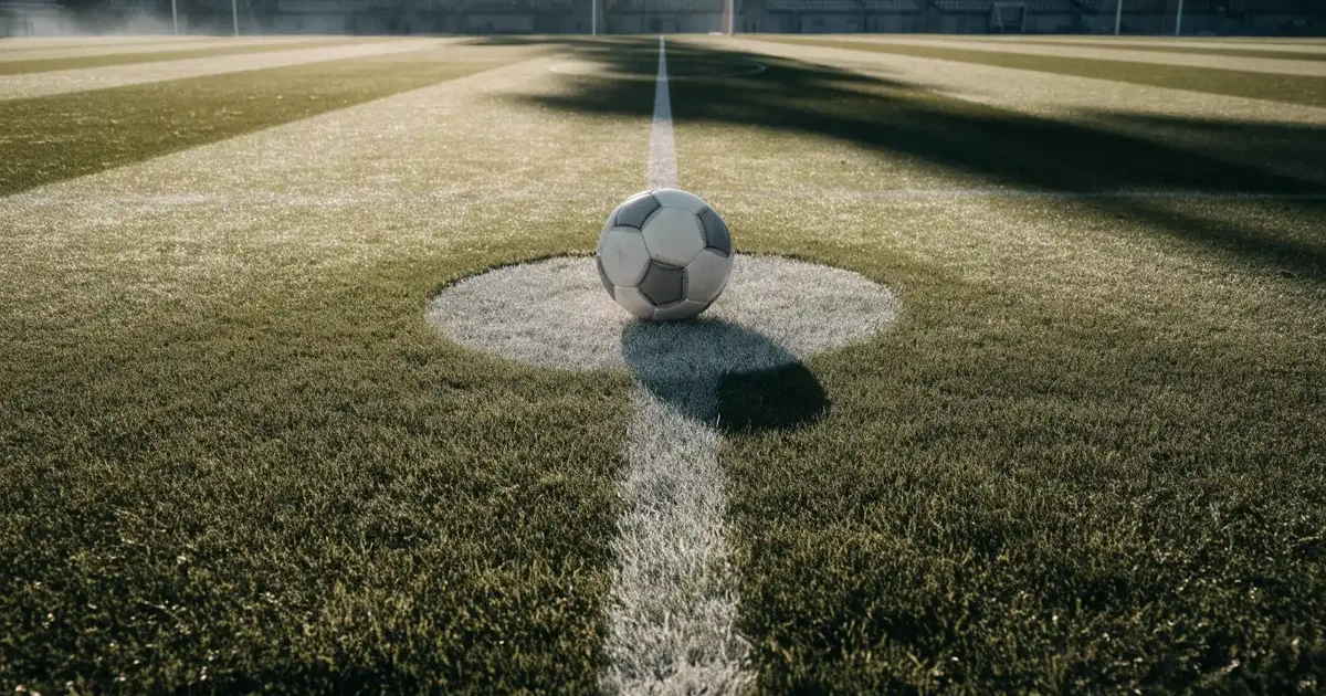 Uma bola de futebol no ponto central de um relvado, à luz da manhã