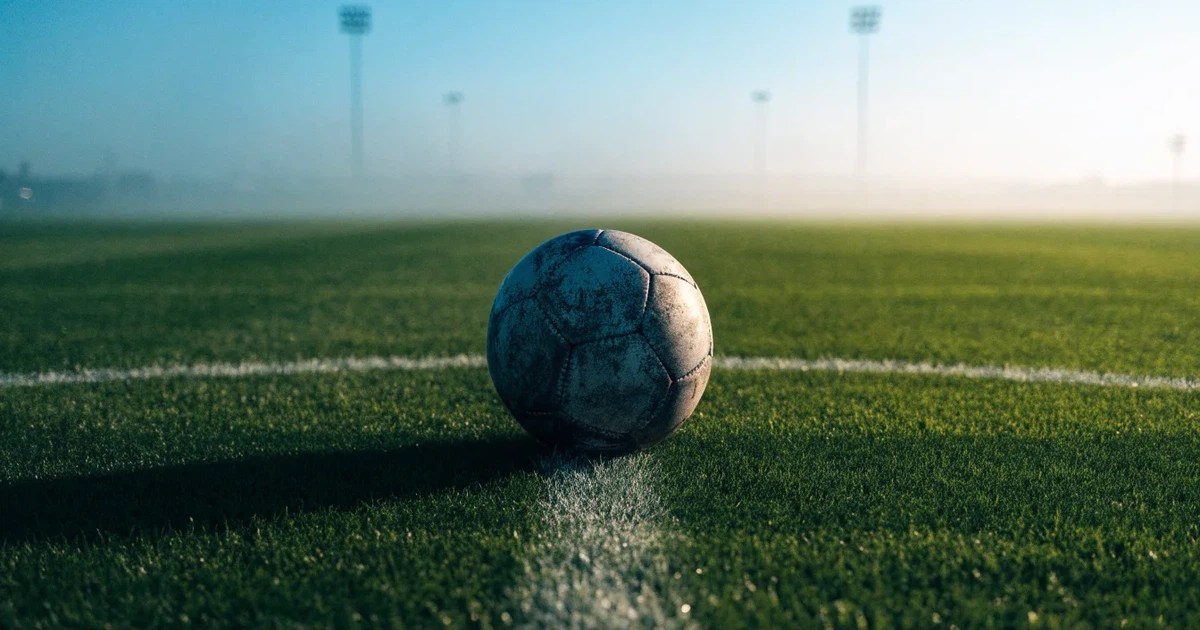 Uma bola de futebol no ponto central de um relvado, à luz da manhã