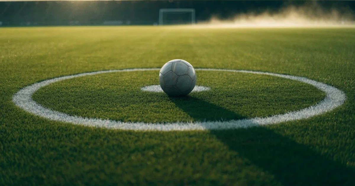 Uma bola de futebol no ponto central de um relvado, à luz da manhã