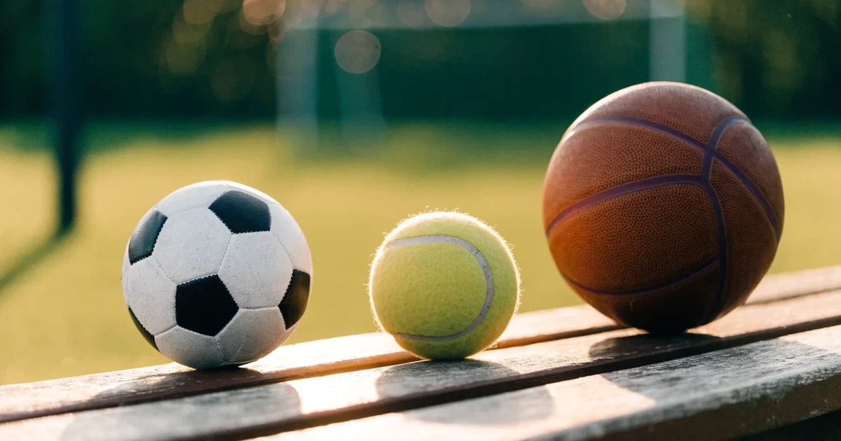 Três bolas de desportos diferentes alinhadas lado a lado num banco de madeira