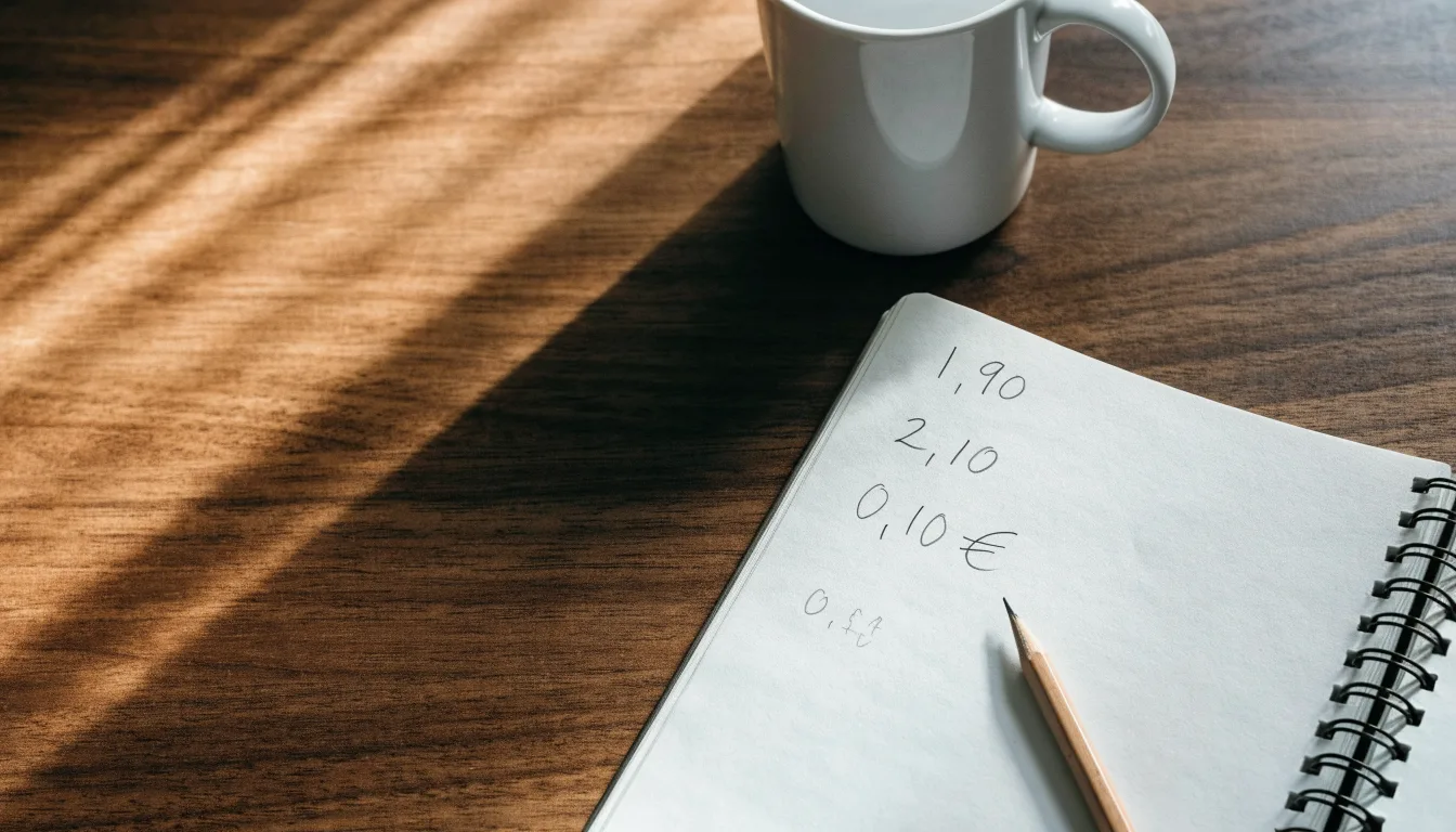 Um caderno aberto com cotas escritas à mão, uma calculadora e um lápis sobre uma mesa de madeira