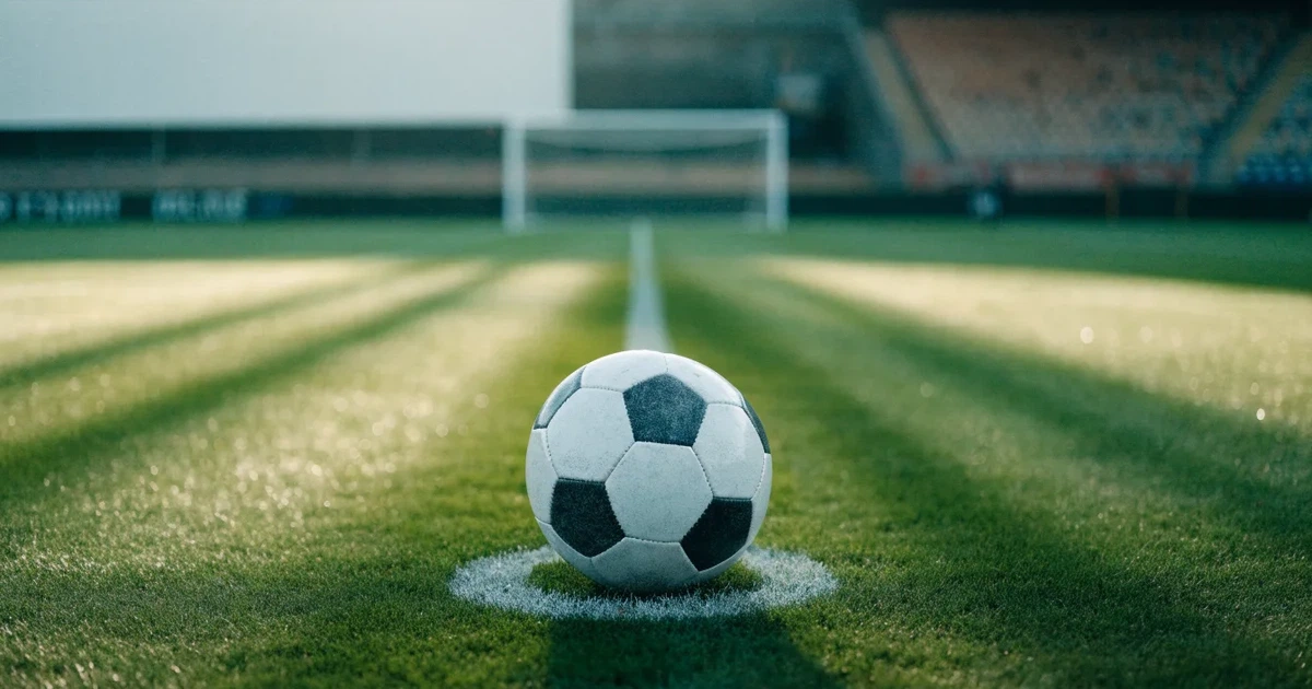 Uma bola de futebol no ponto central de um relvado, à luz da manhã